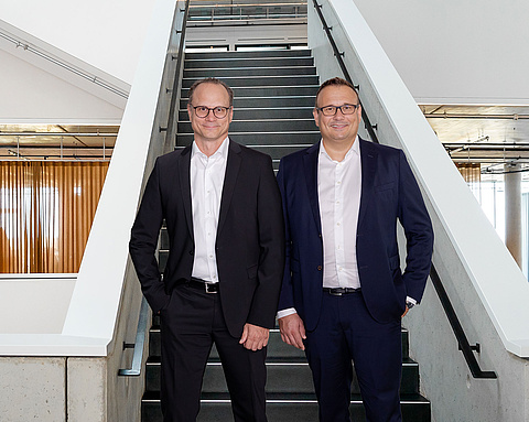 Die Geschäftsführer Michael Huber und Lars Rippert von baramundi stehen vor einer Treppe in einem modernen Bürogebäude