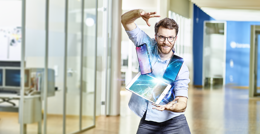 Ein fröhlicher Mann, der mehrere mobile Geräte mühelos in der Luft jongliert, um Enterprise Mobility Management zu demonstrieren